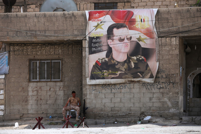 A Syrian soldier sits next to a poster of the Syrian president at the entrance of the Wafideen Camp as they wait for the arrival of buses carrying Jaish Al Islam fighters and their family members evacuated from the Eastern Ghouta town of Douma on Thursday (AFP photo)