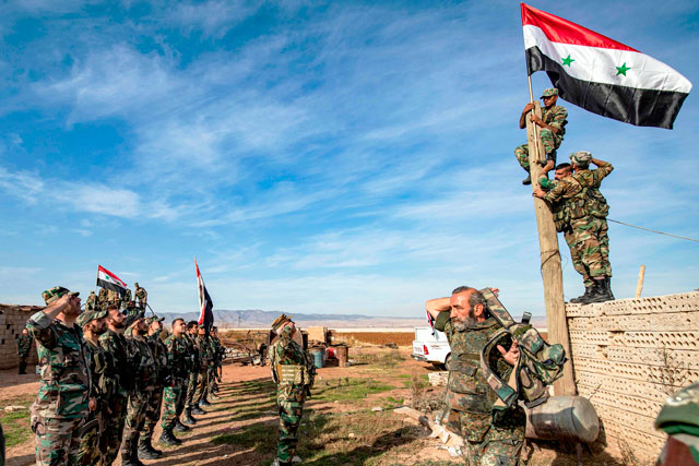 Syrian soldiers perform a salute as others raise up a national flag upon a wooden pole as they deploy for the first time in the eastern countryside of the city of Qamishli in the northeastern Hasakah province on Tuesday (AFP photo)