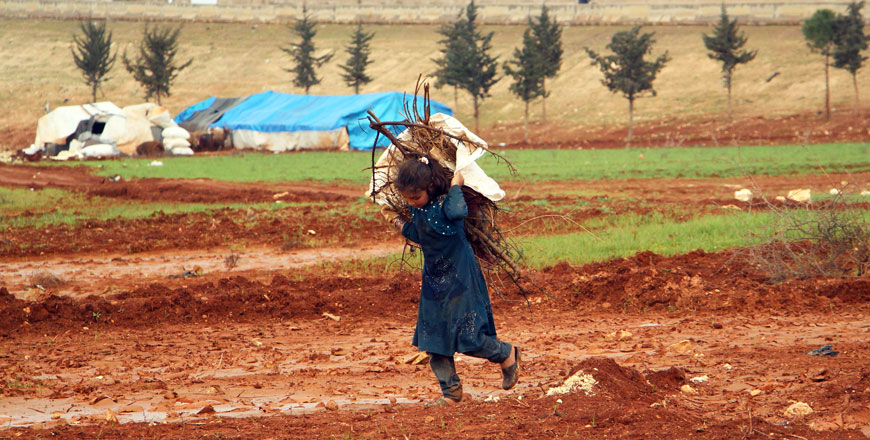 A Syrian girl carries collected branches on her back at a camp for displaced people from the east of Maaret Al Numan, near the cemetary of Kafr Yahmul village north of Idlib in northwestern Syria, on Sunday (AFP photo)
