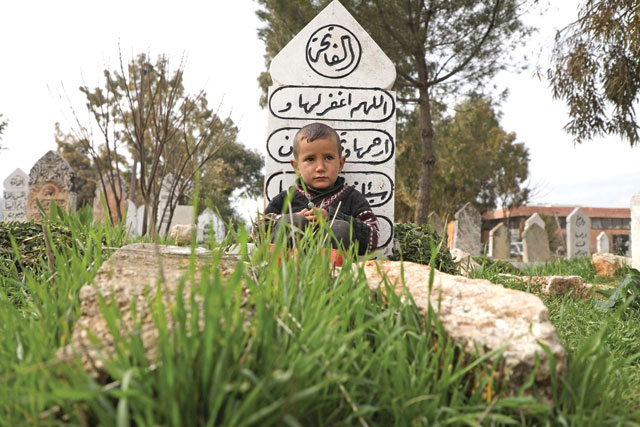 A Syrian boy sits in front of a tombstone at a cemetery where displaced families took refuge in its prayer hall, in the town of Sarmada in Syria's northwestern Idlib province, on February 23 (AFP photo)