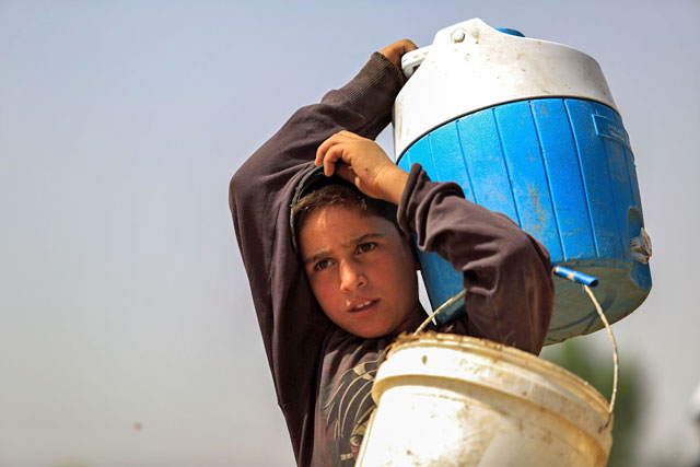 A Syrian boy carries water containers as people harvest wheat in a field near the rebel-controlled town of Hamouria, in the eastern Ghouta region on the outskirts of the capital Damascus, on Sunday (AFP photo)