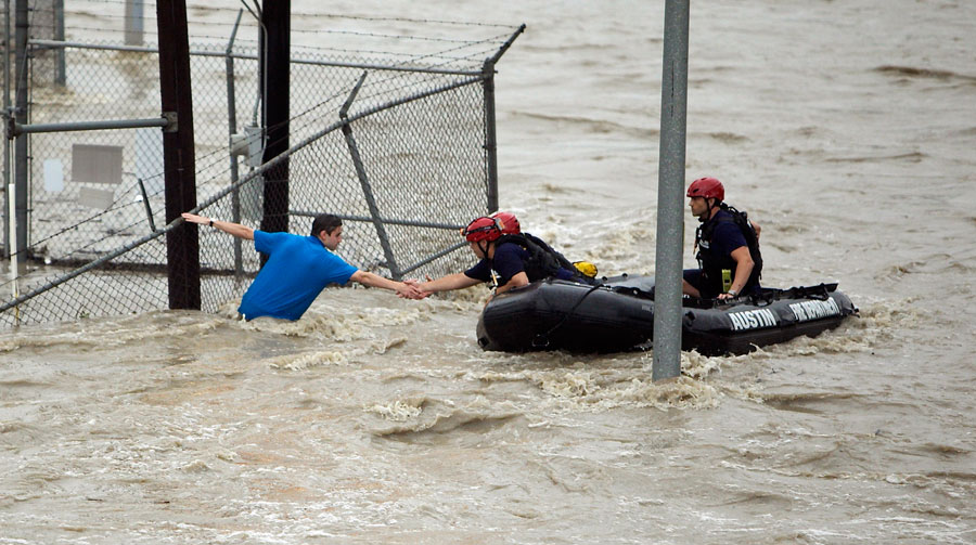 Rescue personnel grab the hand of a man stranded in rushing water at the northwest corner of Lamar Blvd. and 15th St. in Austin, Texas. Shoal Creek overflowed its banks and inundated the major traffic artery with rushing water. Several cars were stalled under and near the 15th St. bridge on Monday (AP photo)