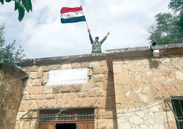 This handout photo released by the official Syrian Arab News Agency on Thursday shows a Syrian government soldier waving a Syrian national flag as he stands atop the customs office building in the Syrian Kurdish town of Kobane (AFP photo)