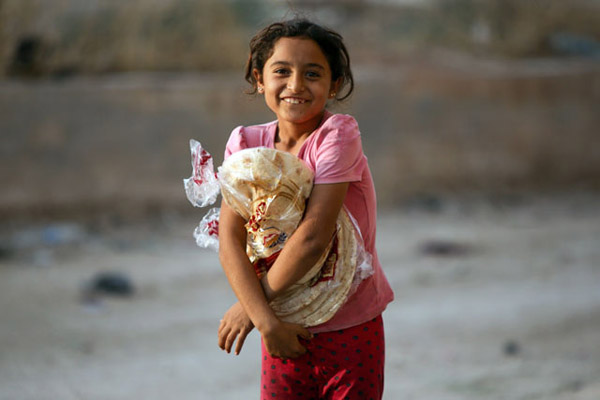 A Syrian girl, displaced due to the ongoing Turkish military operation in northeastern Syria, receives bread from a Turkish NGO in the town of Ain Al Arus, south of the border town of Tal Abyad on Friday (AFP photo)