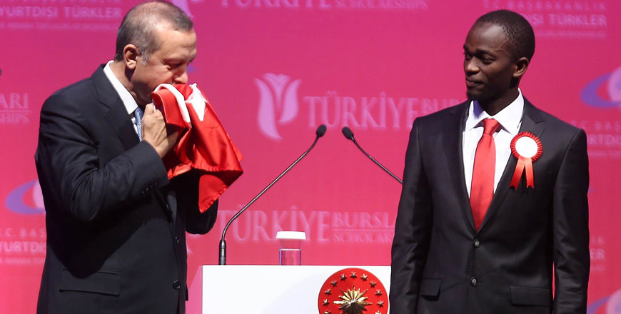 Turkey’s President Recep Tayyip Erdogan kisses a handmade Turkish flag, given to him as a gift from Ugandan university student Cemil (right) during a graduation ceremony in Ankara on Thursday (AFP photo)