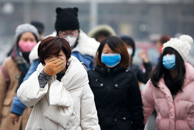 A woman uses her hand to cover her face from pollutants as people walk along a street on a polluted day in Beijing on Tuesday (AP photo)