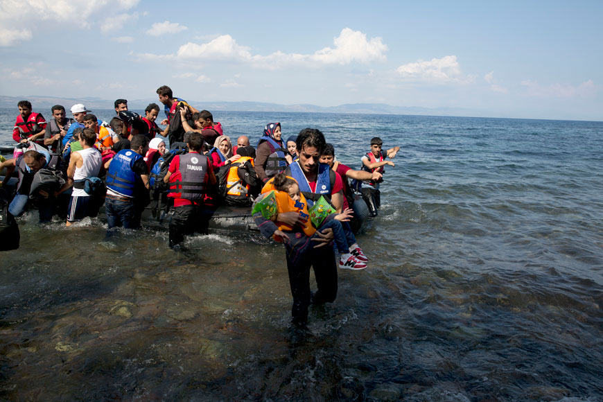 A man carries a child as migrants and refugees arrive on a dinghy after crossing from Turkey to Lesbos Island, Greece, Tuesday (AP photo)