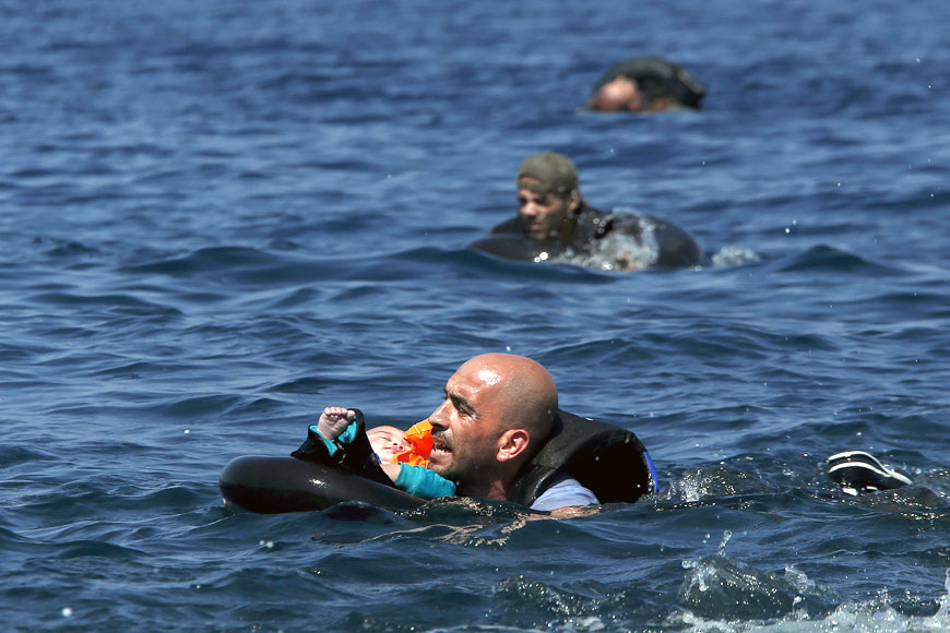 A Syrian refugee holding a baby in a lifetube swims towards the shore after their dinghy deflated some 100 metres away before reaching the Greek island of Lesbos, on Sunday (Reuters photo)