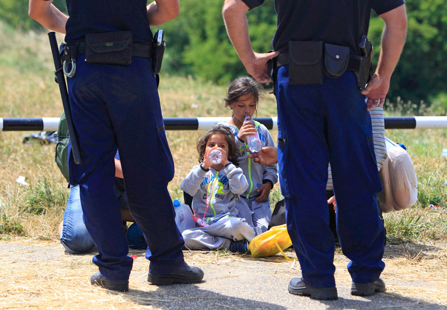 Police guard migrants from Syria who have crossed the border from Serbia to Hungary, walking on the dam near the Tisza River near the city of Szeged, on Monday (Reuters photo)