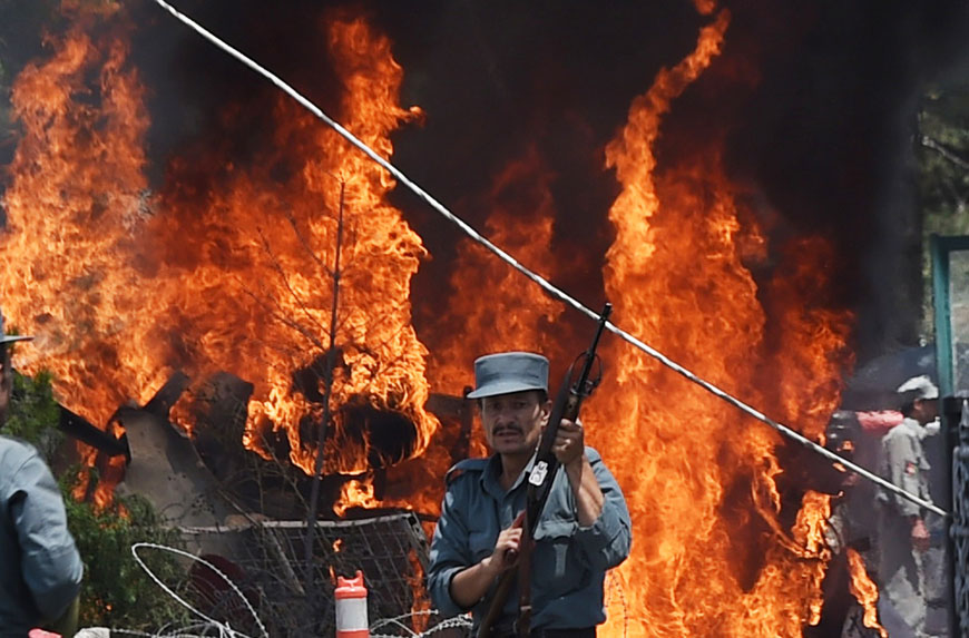 An Afghan policeman stands guard as smoke and flames rise from the site of a huge blast near the entrance of Kabul's international airport, in Kabul on Monday (AFP photo)