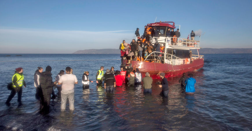 Volunteers help around 150 refugees and migrants, mostly from Syria and Iraq, to disembark from a vessel after their arrival from the Turkish coast to the northeastern Greek island of Lesbo, on Tuesday (AP photo)