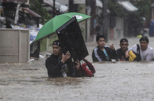 A man (left) carries a television as residents make their way through a flooded street to shelter after Typhoon Vamco hit the area in Marikina City, suburban Manila on Thursday (AFP photo)